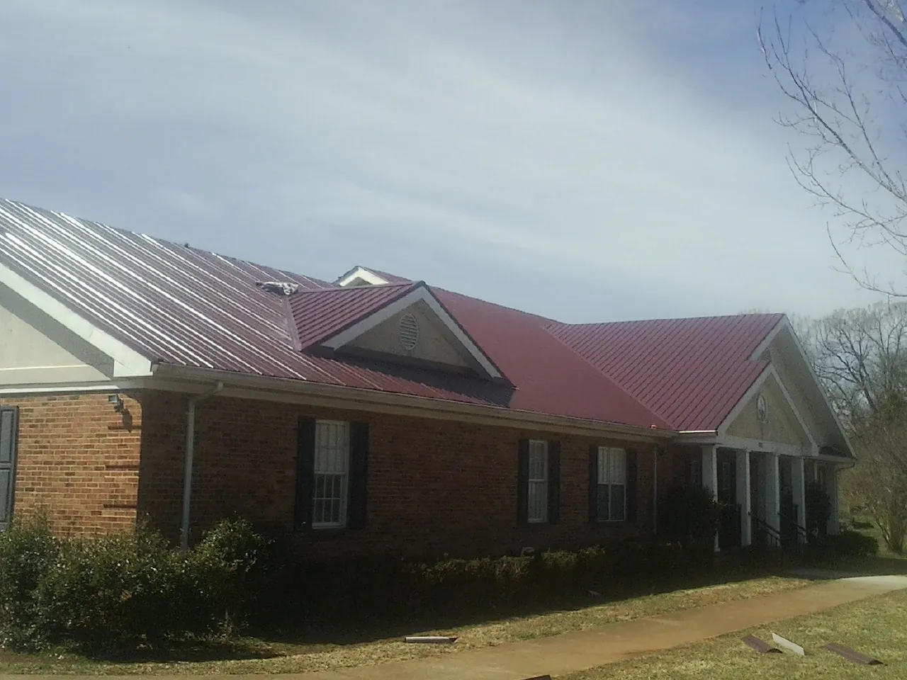 Red metal roof with gabled entries on a long brick building, from a Hail Damage Roof Repair job in Sophia