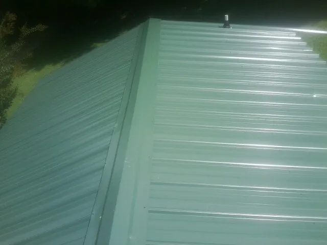 New green metal panels meeting at the ridge of a roof — Flat Roof Repair work by our crew in Sophia