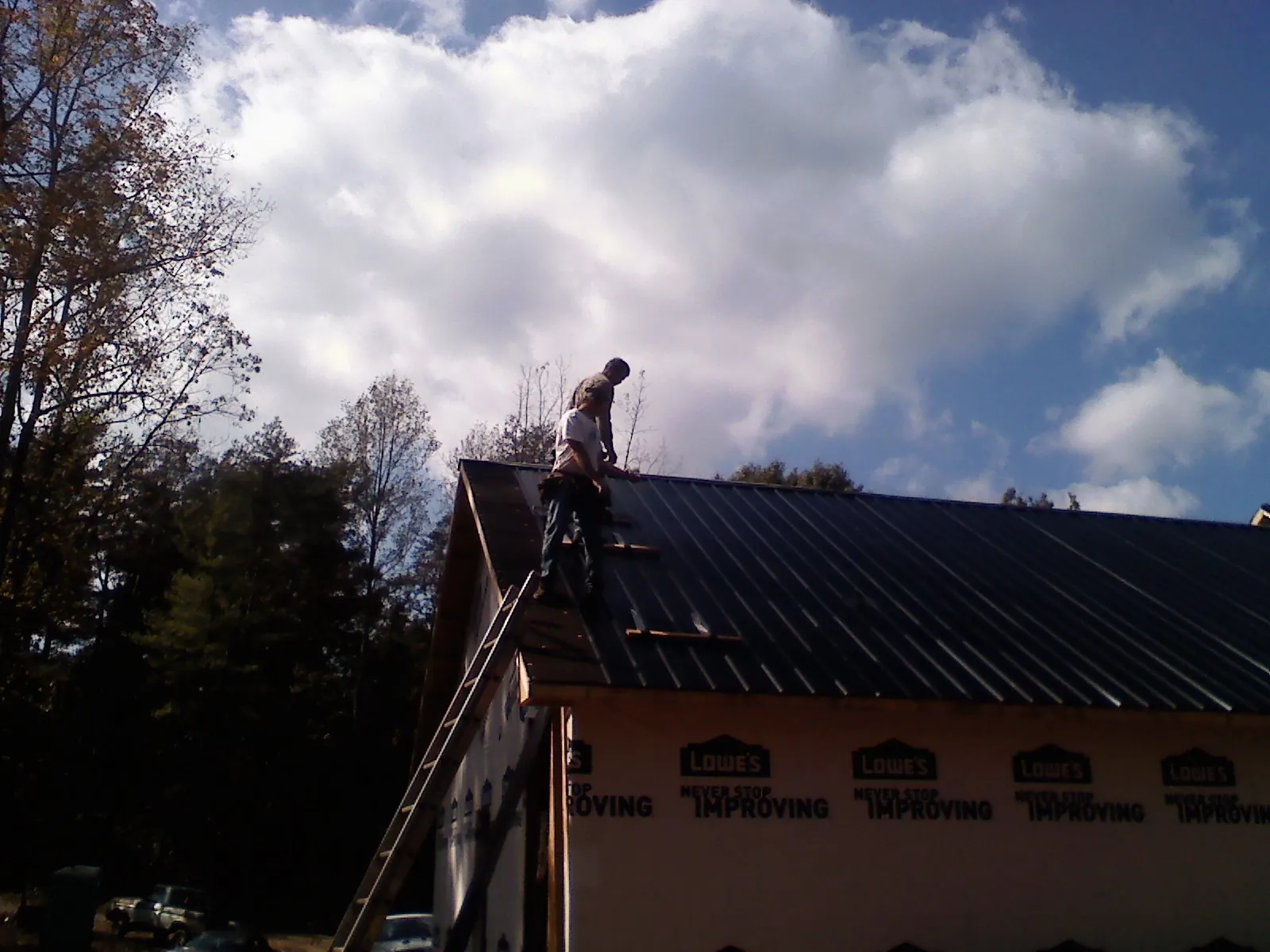 Roofer fastening dark metal panels high against a cloudy sky, from a Roof Inspection job in Sophia