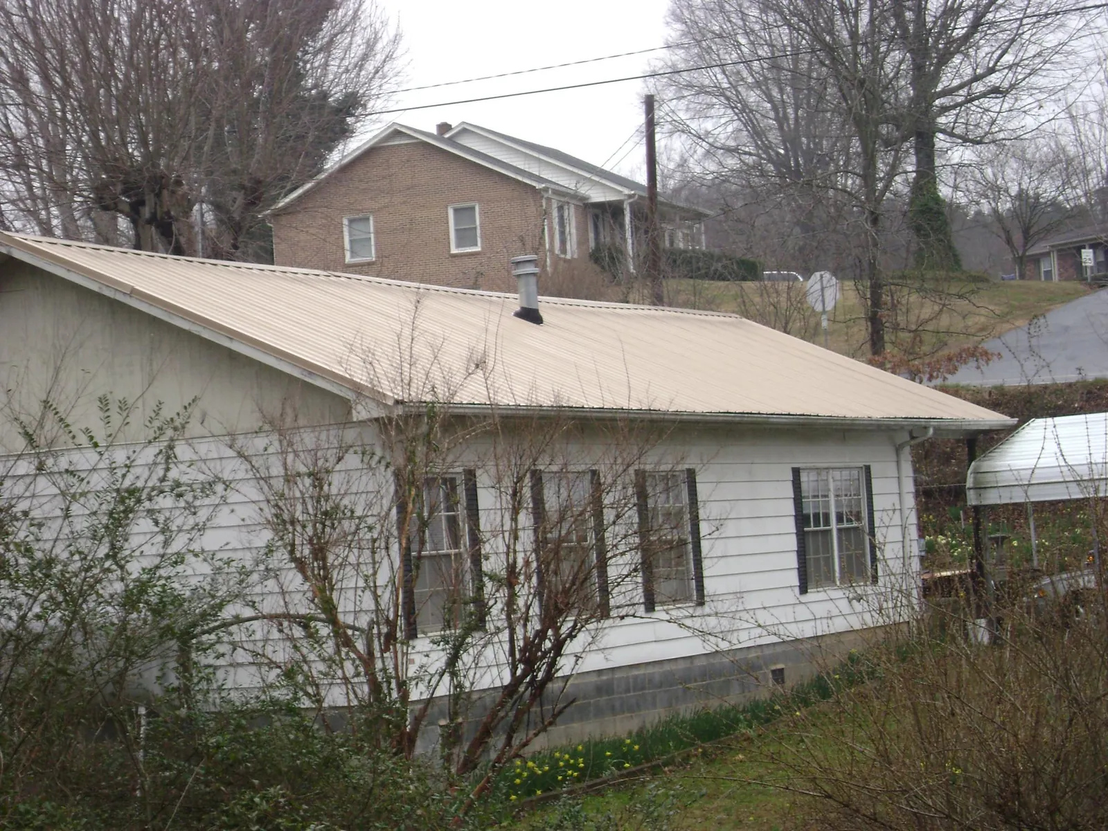 Tan metal roof on a white sided house set into a hillside — Commercial Roofing by Roofing Brothers in Sophia